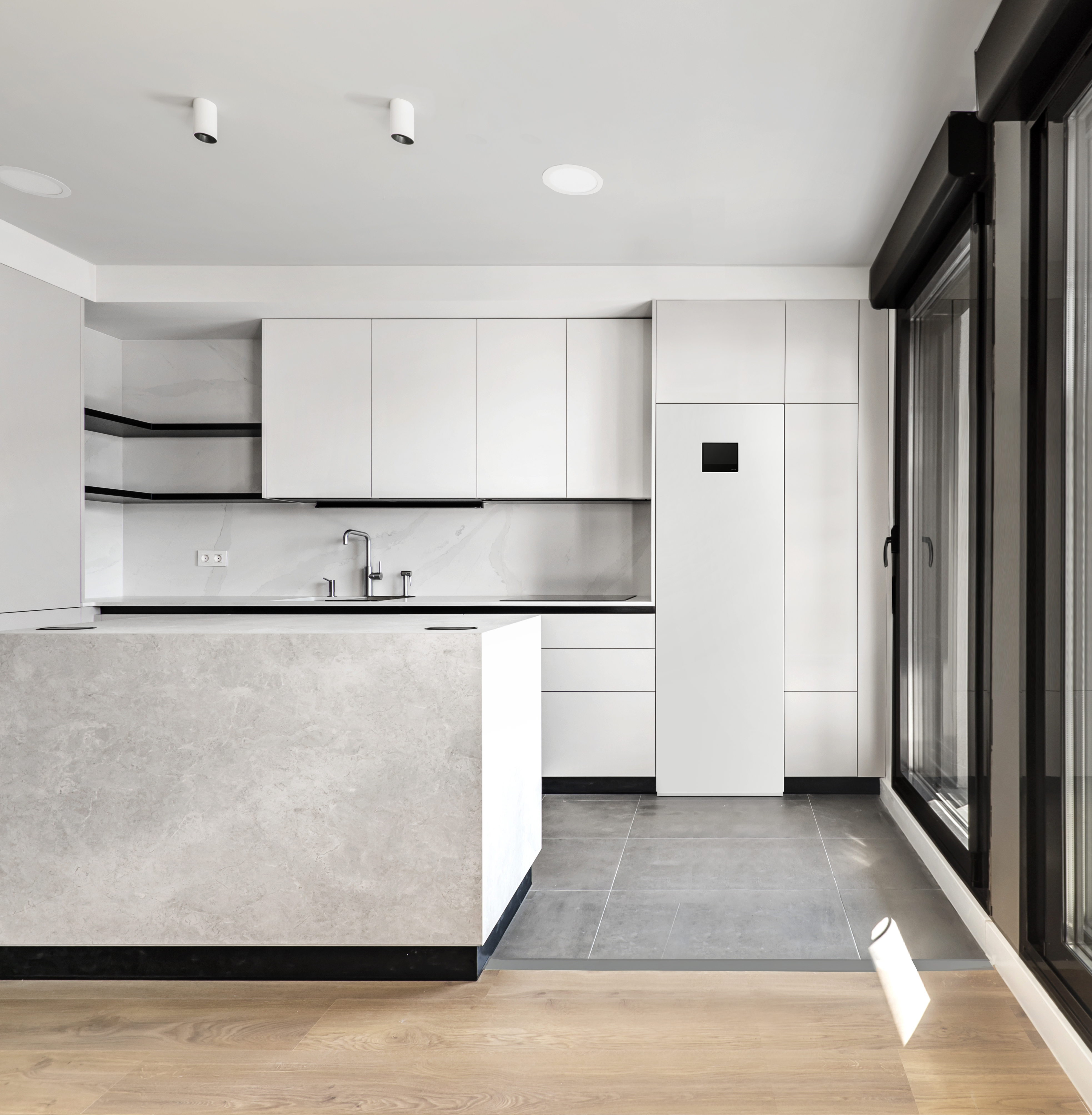 Newly installed modern kitchen with central island, smooth gray cabinets, black glass appliances and glass-covered wall with access to an open terrace
